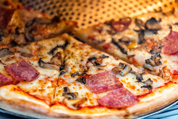 Macro closeup of fresh thin crust round pizza in store cafe on display restaurant with melted mozzarella cheese, pepperoni meat slices and mushrooms