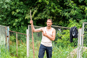 Man in garden cutting weeds oat grass with sickle scythe manual tool in green summer in Ukraine...