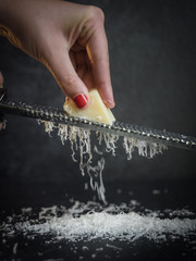 Hand of a woman grating parmesan cheese on a black background. Dark food