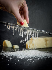 Hand of a woman grating parmesan cheese on a black background. Dark food