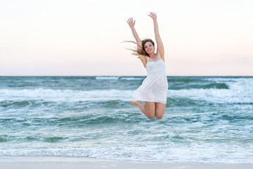 Young happy smiling woman in white dress on beach sunset in Florida panhandle with ocean waves...