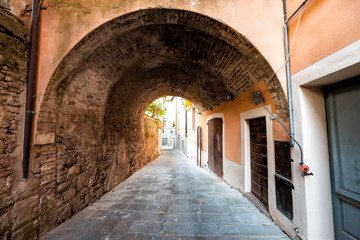 Fototapeta na wymiar Chiusi, Italy street in small historic medieval town village in Umbria during sunny day with nobody orange yellow pink colorful walls and arch