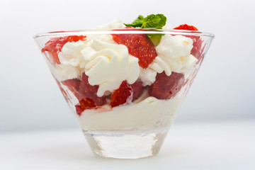 juicy strawberries with cream and a sprig of mint in a transparent glass bowl on a white background side view