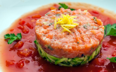 Tartar beefsteak with fresh cucumbers and tomato sauce in a white plate close-up
