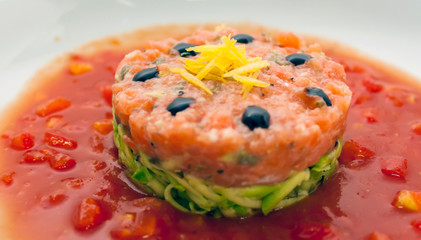 Tartar beefsteak with fresh cucumbers, olives and tomato sauce in a white plate close-up