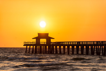 Naples, Florida yellow orange sunset closeup in gulf of Mexico with sun and Pier wooden jetty...