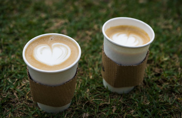 Close up of latte cappuccino coffee cup with frothed milk in heart shape against natural grass background
