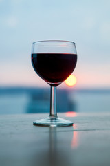 A glass of red wine in front of the beautiful soft sunset. Romantic dinner on the beach.