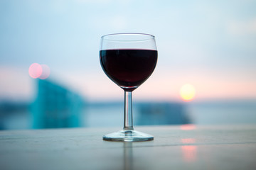 A glass of red wine in front of the beautiful soft sunset. Romantic dinner on the beach.