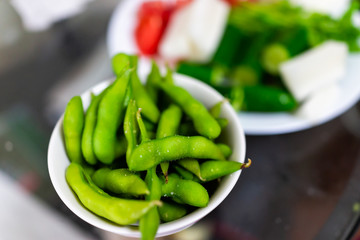 Traditional japanese plate in restaurant or house with vegetable dish snack of boiled edamame with salt and vegetables, green color closeup