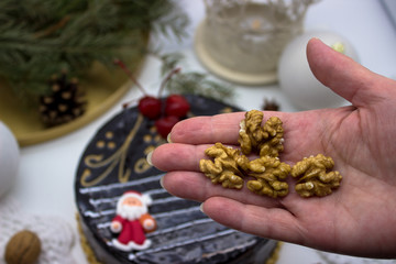 A hand that holds walnuts. In the background, a delicious chocolate cake decorated with cherries and Christmas decorations.
