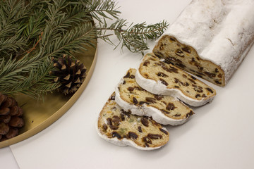 The three slices and the main part of Stollen with Christmas ornaments on a white background. Traditional German Christmas cake with marzipan and dried fruits.