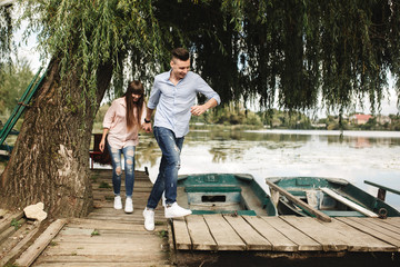 Happy young couple outdoors. young love couple running along a wooden bridge holding hands. love story at the lake. Totally in love. 
