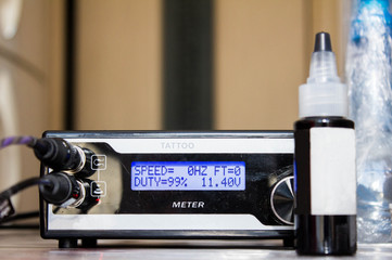 Black power supply for tattoo machine plugged in and bottle with black pigment and white label for...