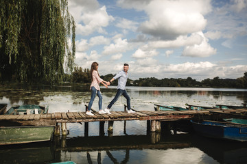 Naklejka premium Totally in love. Happy young couple outdoors. young love couple running along a wooden bridge holding hands. love story at the lake