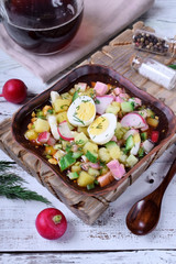 Russian cold soup Okroshka with vegetables, sausage, eggs and kvass in a ceramic bowl on the white table