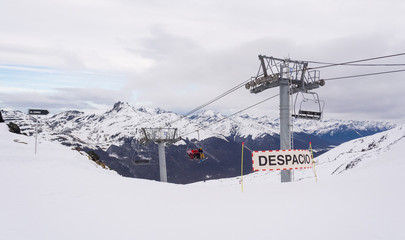 Fototapeta na wymiar View of a ski slope with some warning signs and a chairlift on Castor ski center, on a cloudy winter day, with a mountain range on the background. Ushuaia, Tierra del Fuego, Argentina