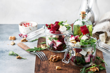 Beet salad with arugula, cheese and walnuts, summer salad jar, gray kitchen table background, copy space, selective focus