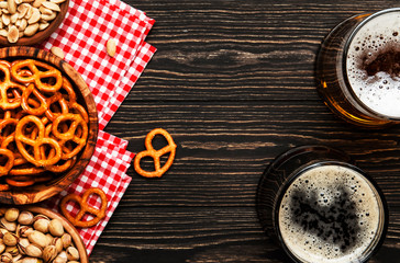 Light and dark beer in mugs and salty snacks and nuts, dark wooden table, frame with copy space, top view