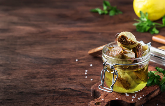 Artichokes in olive oil, glass jar, rustic wooden table, still life, copy space, selective focus