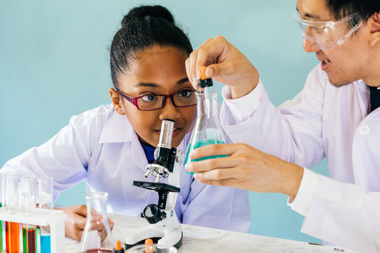 Male Asian science teacher teaching and doing chemistry lab test to curious African American elementary student - education for kids concept