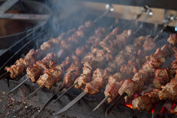 Traditional Caucasian BBQ shashlik grilled meat on sticks being cooked on open fire with smoke, close up view - 265520862