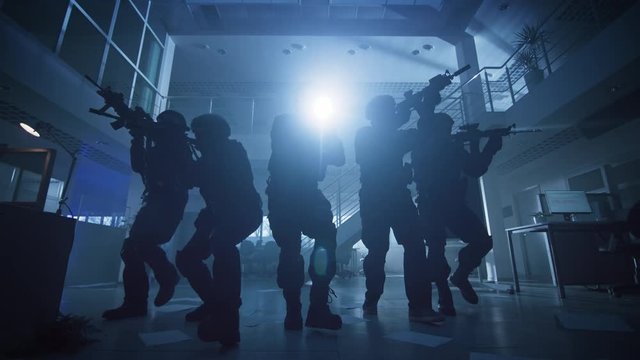 Masked Squad of Armed SWAT Police Officers Slowly Move in a Hall of a Dark Seized Office Building with Desks and Computers. Soldiers with Rifles and Flashlights Surveil and Cover Surroundings.