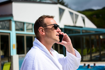 Man enjoying wellness spa resort treatments.  A young businessman speaks with a smartphone on the terrace of an exclusive spa center at afternoon.