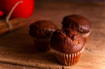 Fresh chocolate muffins and cinnamon sticks on rustic wooden background