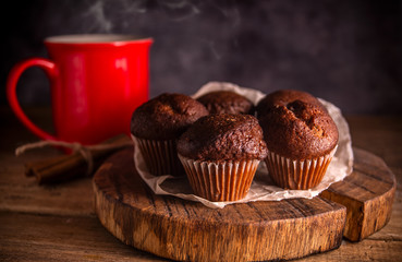 Fresh chocolate muffins and cinnamon sticks on rustic wooden background