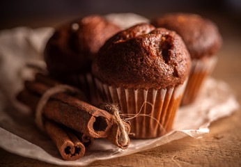 Fresh chocolate muffins and cinnamon sticks on rustic wooden background