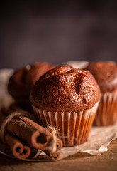 Fresh chocolate muffins and cinnamon sticks on rustic wooden background