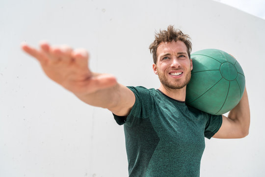 Medicine ball heavy weighted ball workout man training in outdoor gym. Body toning core workout doing lunge squats, holding weight on side shoulder. Male athlete doing strength training exercises.