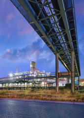 Scaffold with pipeline and Illuminated petrochemical production plant at twilight at Port of Antwerp.