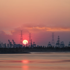Fototapeta na wymiar Riverbank with silhouettes of container terminal cranes during a red colored sunset, Port of Antwerp, Belgium.
