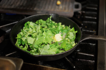 Chopped greens being sauteed with butter in a cast iron pan in a restaurant kitchen