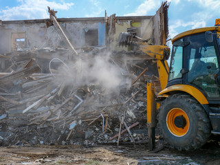 Destruction of walls of old building and cleaning of construction debris with bucket of...