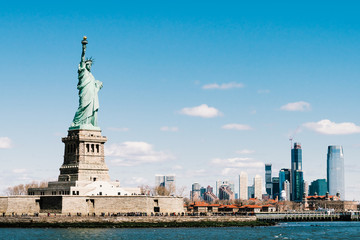 Statue of Liberty on sunny day with New York city Manhattan island in background. America cityscape, United States nation symbol, travel destination or tourist attraction concept