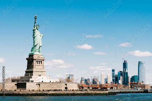 Statue of Liberty on sunny day with New York city Manhattan island in background. America cityscape, United States nation symbol, travel destination or tourist attraction concept