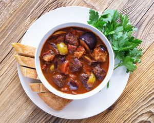 braised veal and red wine stew with tomatoes, olives, eggplant, spices, and herbs served with white bread and fresh parsley on wooden top