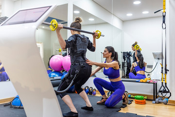 EMS electro stimulation women exercises with trainer coach.  Female athlete wearing ems workout top and strapped to heart monitors.  Exercising in fitness studio and wearing ems outfits