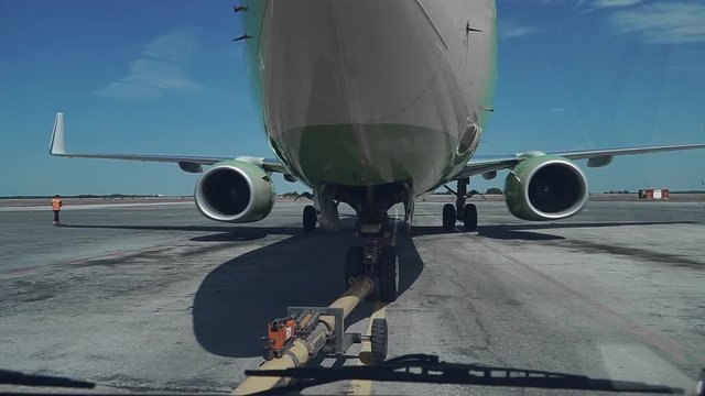 Pushback of a passenger aircraft at the airport in hangar. The airplane nose, landing gear and towing truck close up. 4k