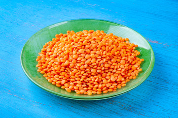 Red lentils in a green plate on a blue wooden background.