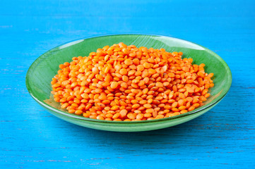Red lentils in a green plate on a blue wooden background.