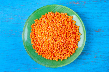 Top view red lentils in a green plate on a blue wooden background.