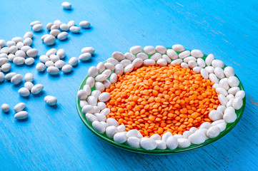 Red lentils and white beans in a green plate on a blue wooden background.