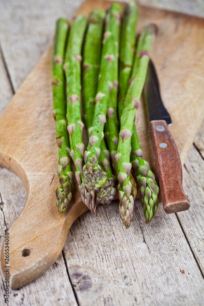 Wall mural fresh raw garden asparagus and knife closeup on cutting board on rustic wooden table background.