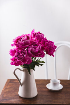 Pink peonies in a pitcher on a wooden table