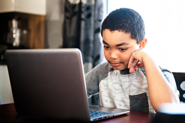 Black boy sitting playing on a laptop computer at home