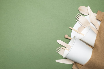 The concept of eco-friendly disposable tableware made of paper and wood on a green background. Top view.  